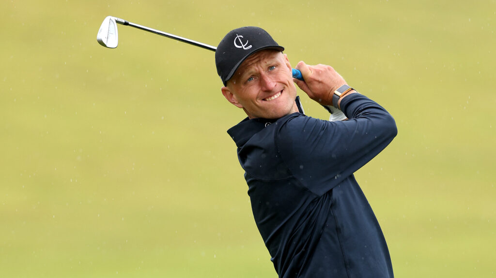 Adrian meronk tittar efter en golfboll med en järnklubba i händerna.