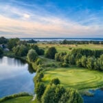golfbana med skog, gräs och sjö fotad från luften