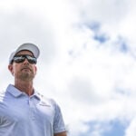 golfspelaren henrik stenson i vit golfkeps och ljus golfpiké. blå himmel och stora vita moln