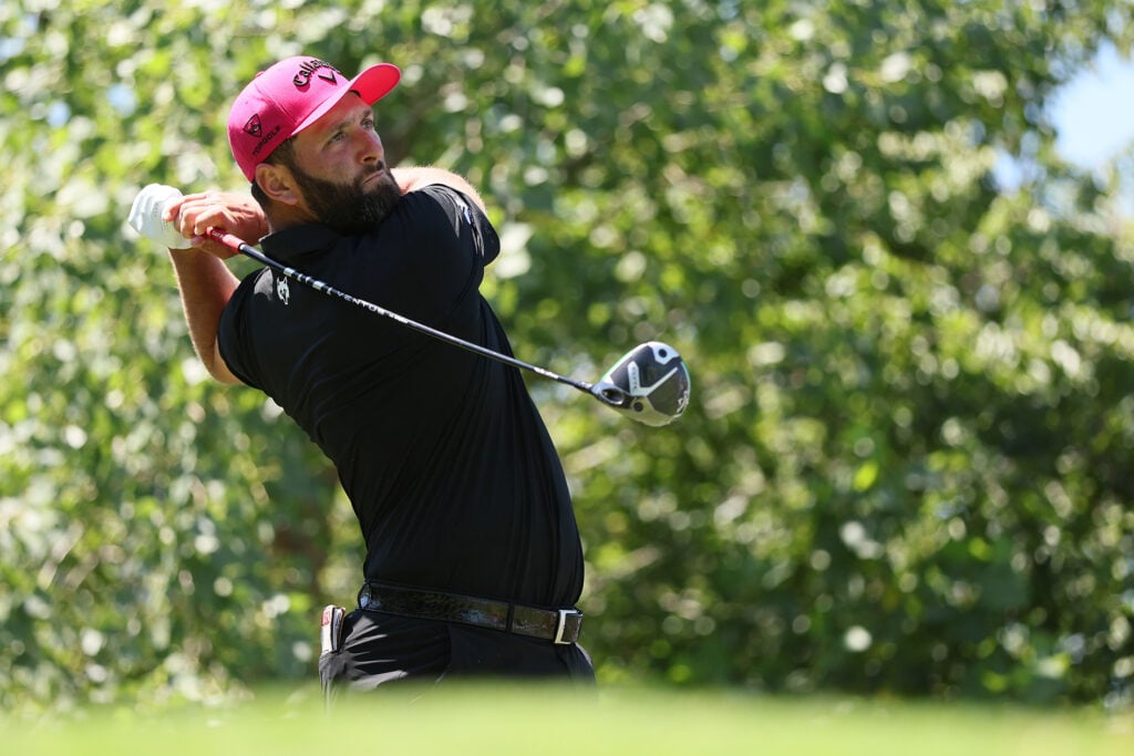 golfspelaren jon rahm i svarta golfkläder och rosa golfkeps på en amerikansk golfbana med ståtliga lövträd