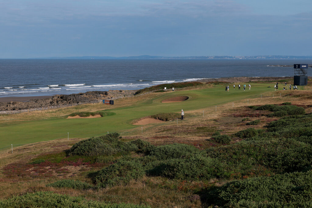 Royal Porthcawl Golf Club i wales med hav i fonden och grön linksbana i förgrunden med kort, mellanhögt, och högt gräs.