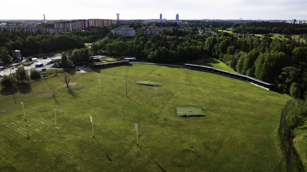 golfanläggning fotad med drönare med stadsmiljö i bakgrunden