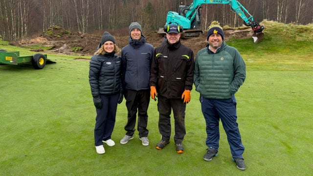 fyra personer i höstkläder på en golfbana framför en turkos grävmaskin