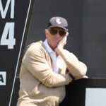 golfspelaren greg norman i solglasögon lutande mot en svart skylt med vit text