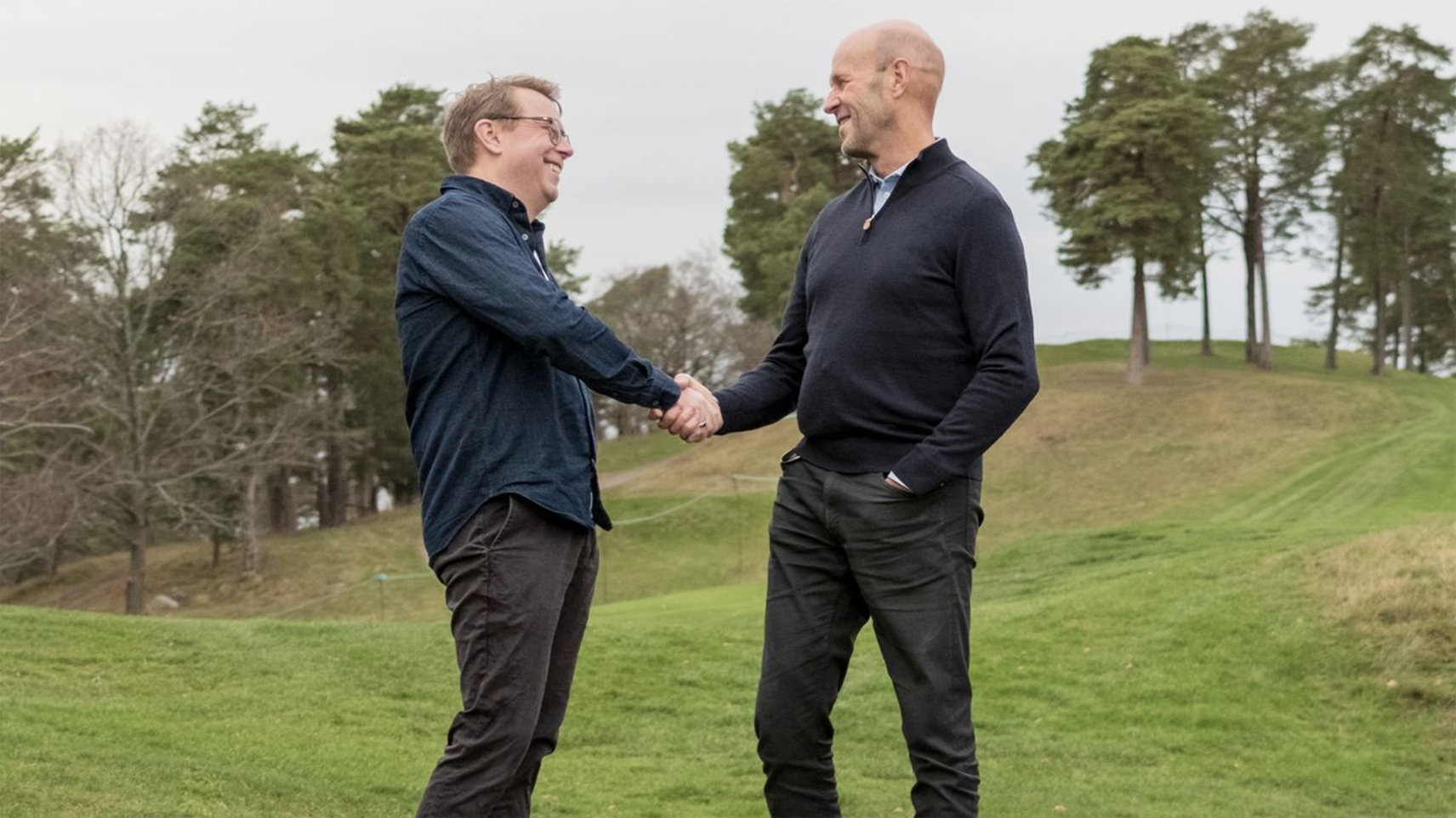 två män skakar hand på en golfbana