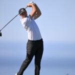golfspelaren ludvig åberg i vit golfpiké och svarta golfbyxor vid havet