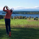 golfspelare på grön golfbana med berg och insjö i horisonten