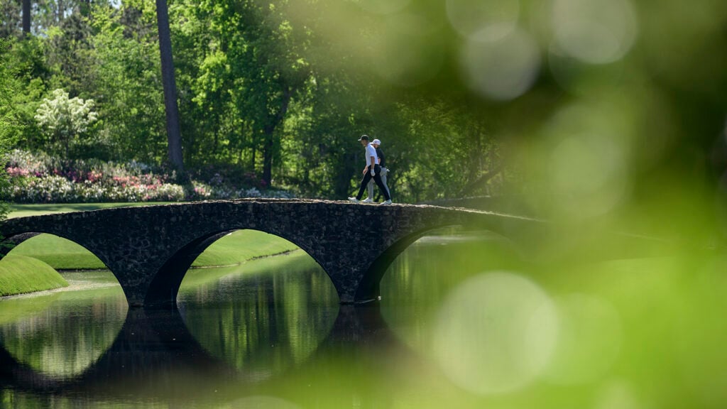 golfspelare går över stenbro över bäck på golfbana