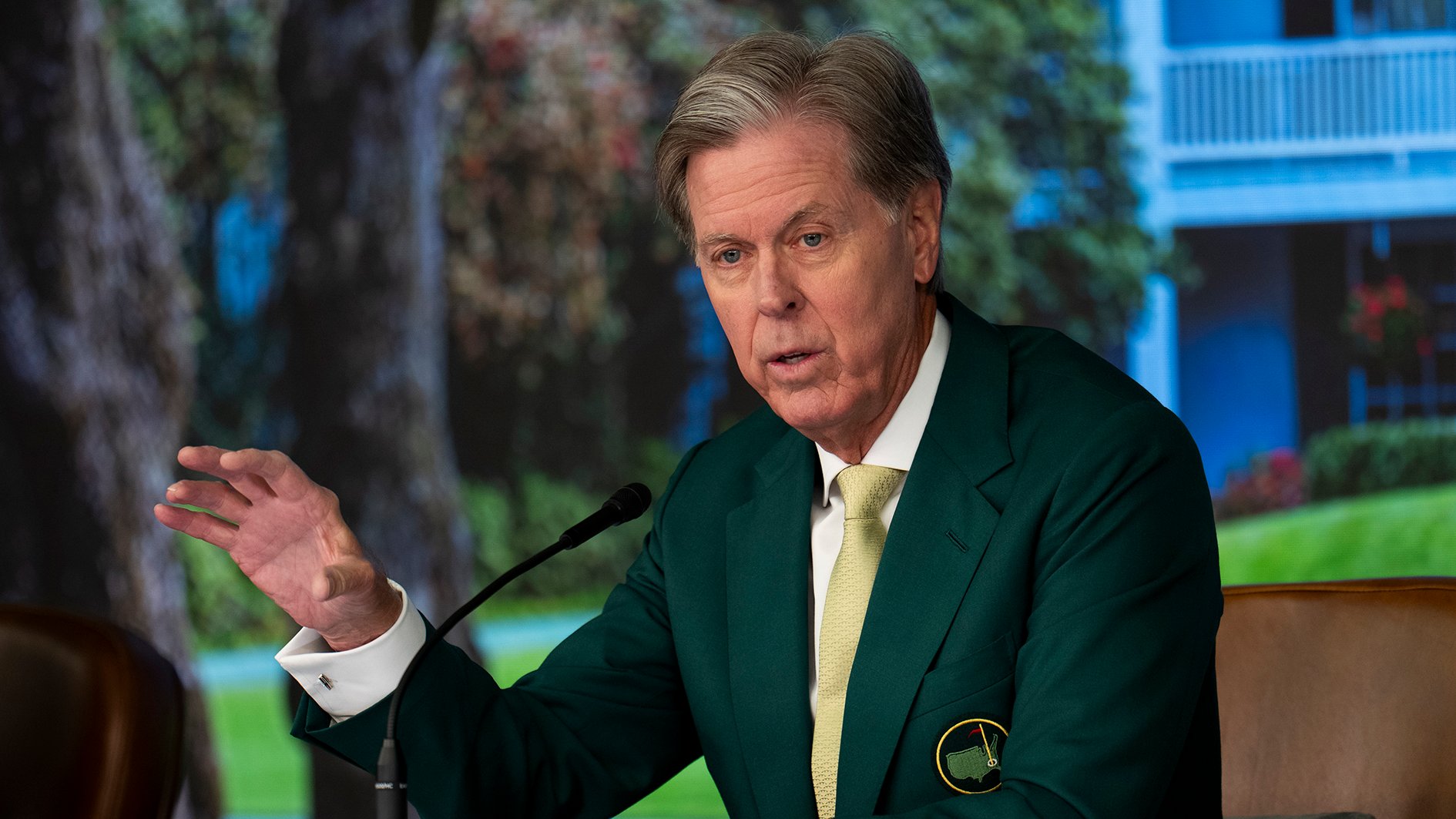 man i grön kavaj pratar i mikrofon på podium