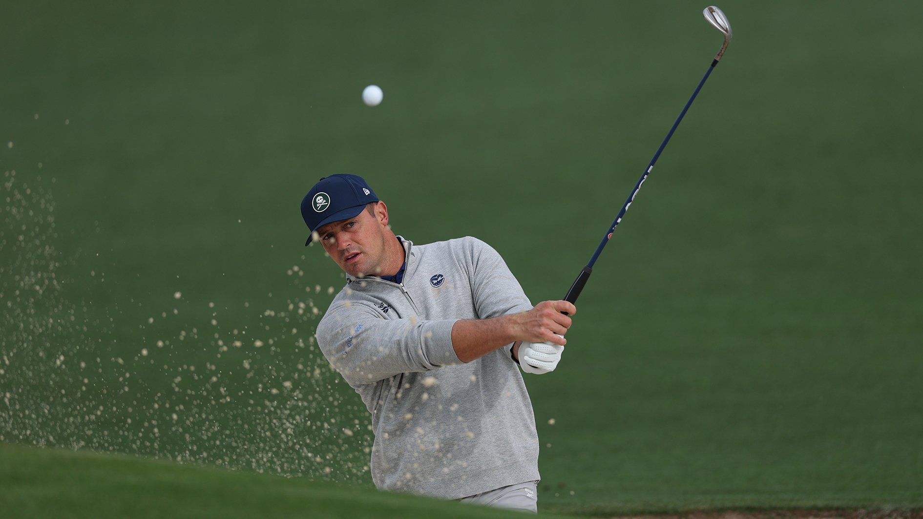 golfspelaren bryson dechambeau slår ett bunkerslag så sand flyger ur bunkern på en golfbana