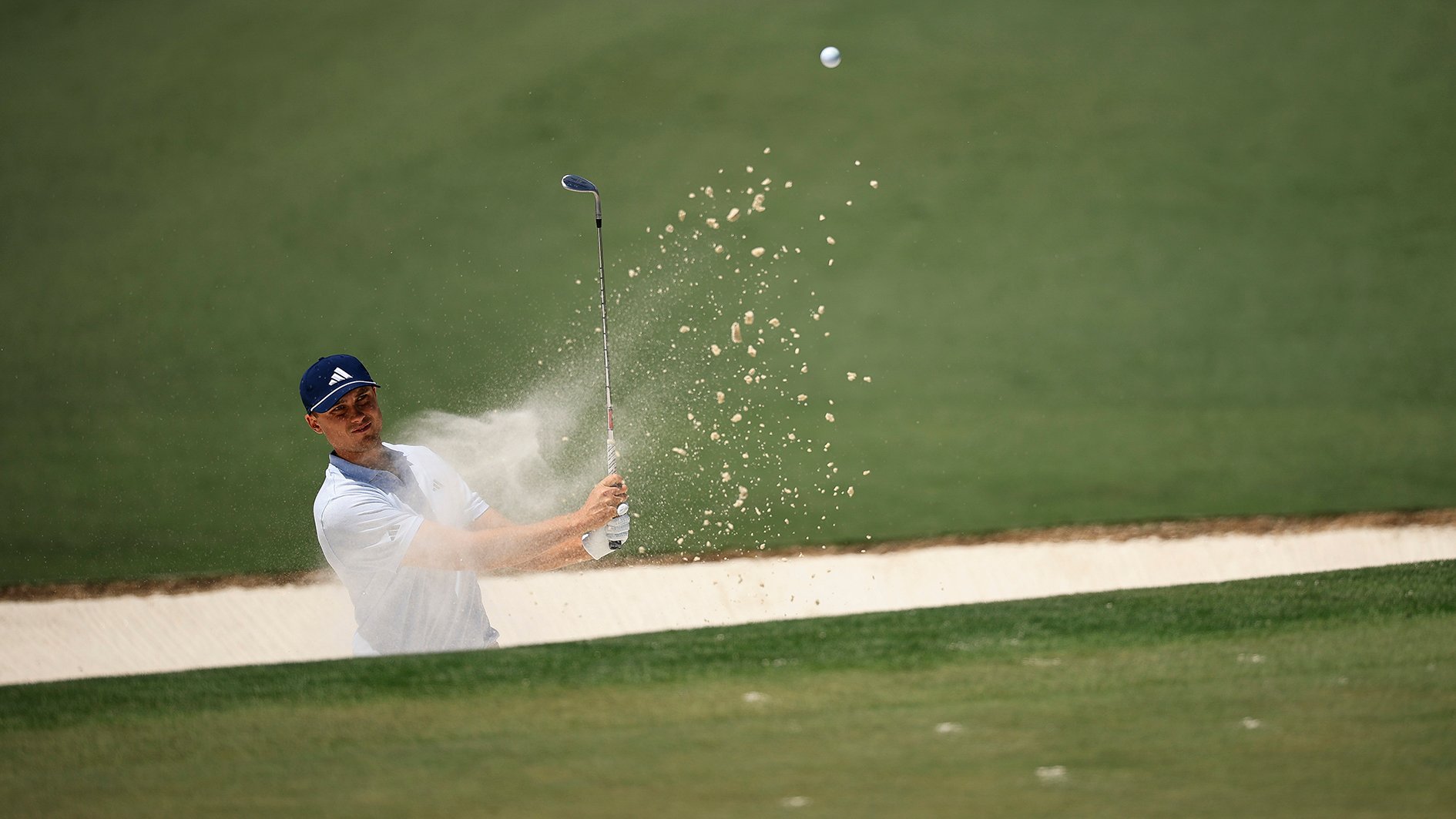 golfspelaren ludvig åberg slår ett bunkerslag på en golfbana så att sanden stänker