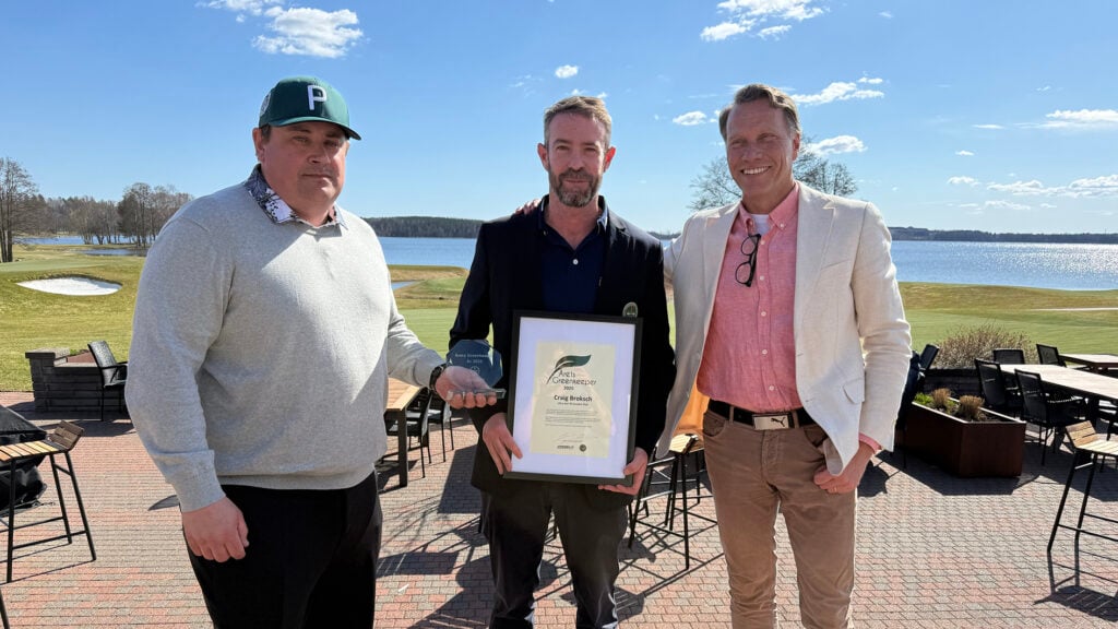 tre män på en golfbana, en tar emot ett diplom