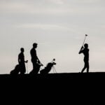 Three boys on the tee box in silhouette.