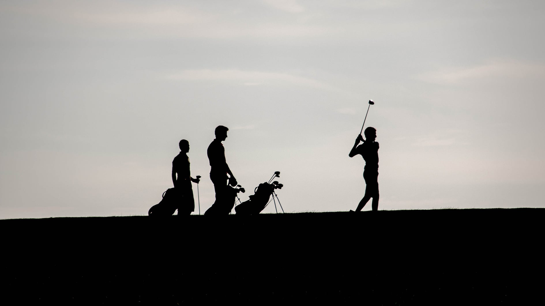 Three boys on the tee box in silhouette.