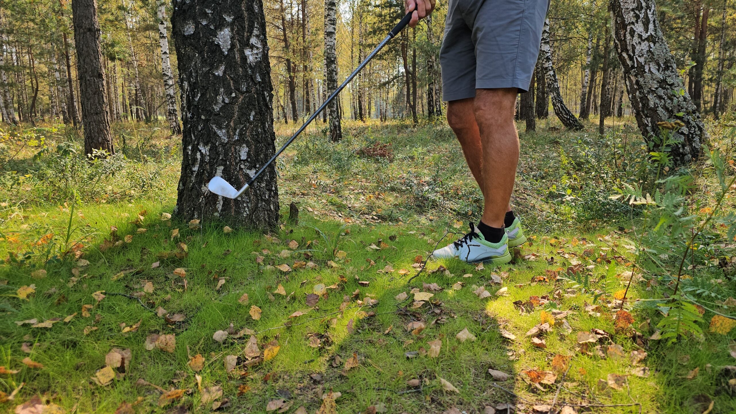 golfspelare slår golfslag från gräs bland lövträd