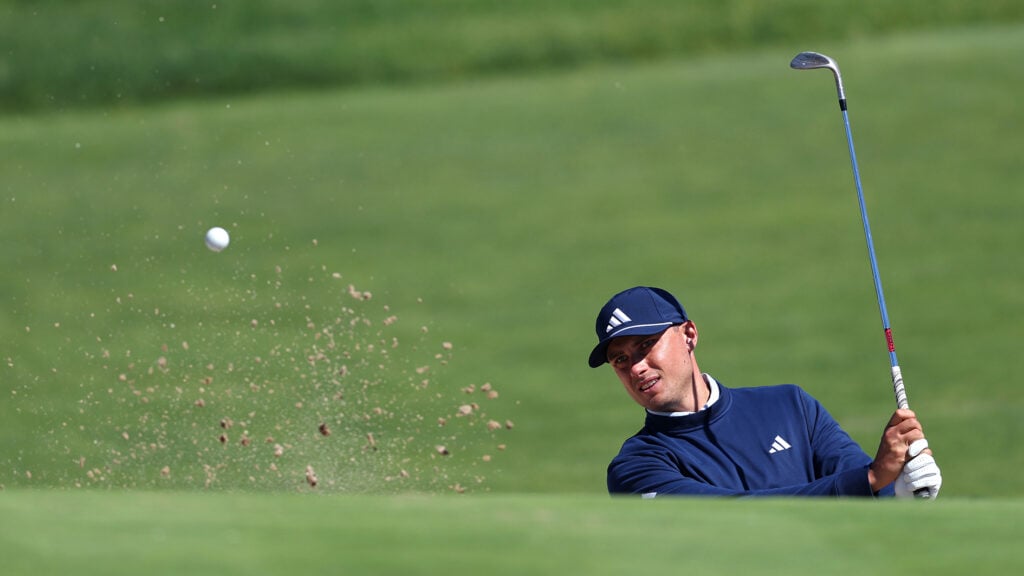 golfspelare slår upp sand och boll ur en bunker
