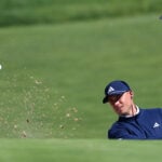 golfspelare slår upp sand och boll ur en bunker