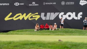 golfspelare sitter i gräset på en golfbana nedanför en läktare.
