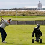 golfspelare på golfbana vid vatten och industriområde