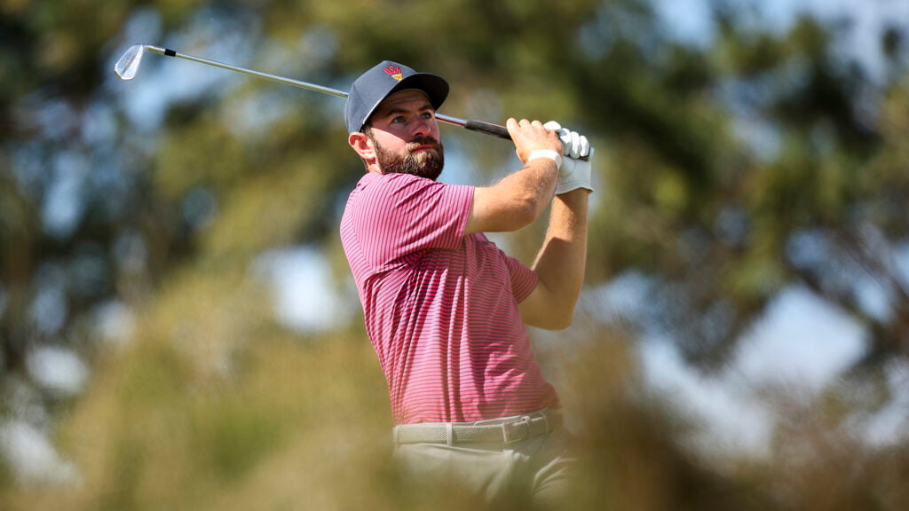 golfspelare slår med järnklubba på golfbana med många träd