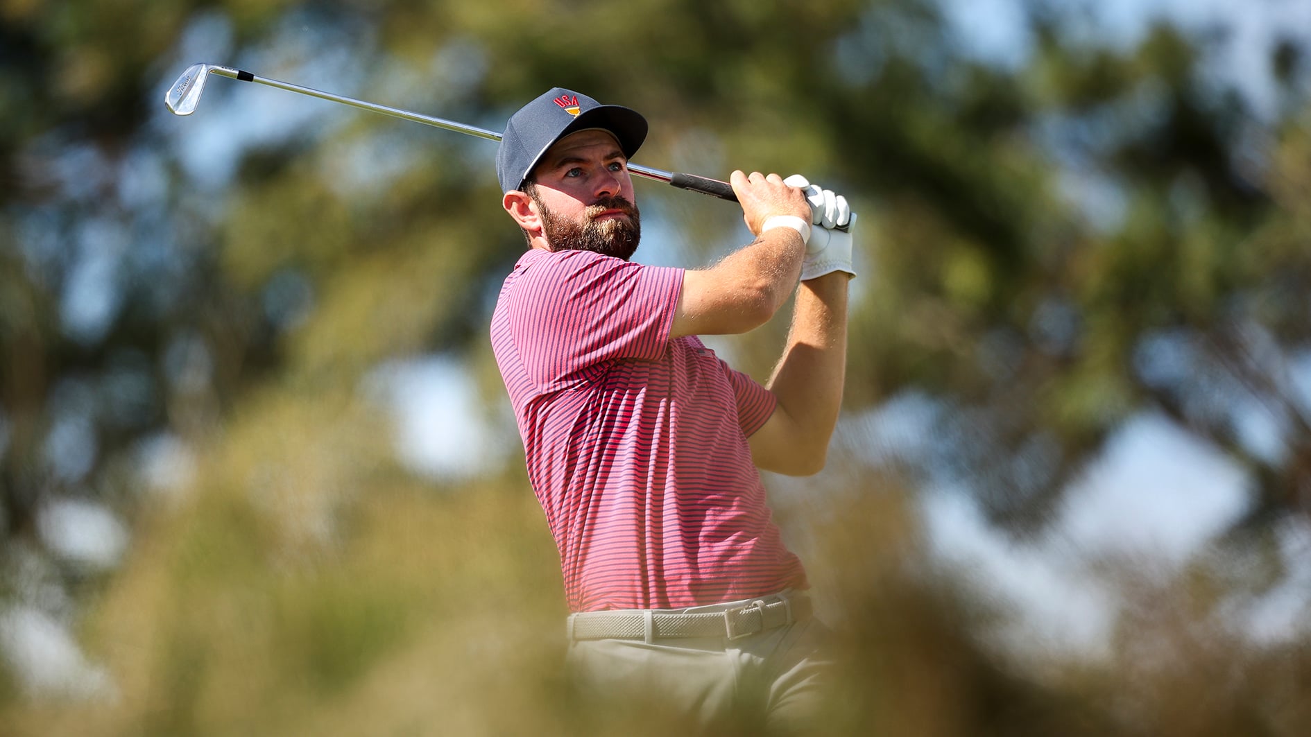 golfspelare slår med järnklubba på golfbana med många träd