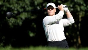 golfspelaren maja stark i vit golftröja slår med golfdriver på golfbana med många buskar